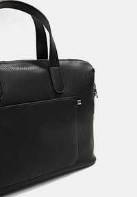 Schwarze Ledertasche für Laptop mit strukturierter Oberfläche, Reißverschluss, zwei Griffen und einer Fronttasche mit dezentem Logo und gestreiften Akzenten.