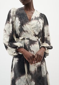 Rochie tip wrap dintr-un material ușor, cu un model floral negru și crem și dungi verticale. Mâneci lungi, bufante și talie legată.