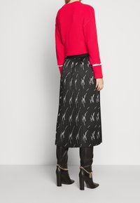 Maglione rosso a coste con maniche lunghe, abbinato a una gonna nera plissettata con un motivo bianco e stivali neri alti con tacco.