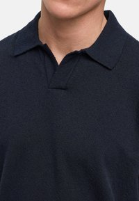 Marineblå polo skjorte laget av teksturert stoff, med klassisk krage og en delvis knappestolpe ved halsen.