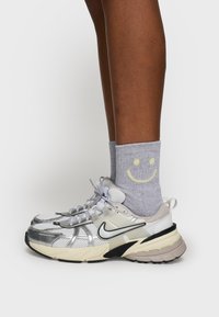 Sneakers z siateczkowymi górnymi częściami w kolorze srebrnym, czarnymi akcentami, kremową podeszwą, zestawione z szarymi skarpetkami z żółtą buźką.