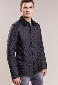 Casaco preto acolchoado com gola de veludo, botões de pressão e bolsos laterais. Apresenta uma superfície texturizada e um design ajustado.