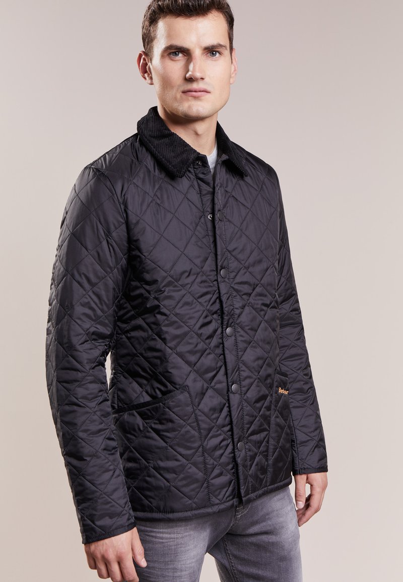 Casaco preto acolchoado com gola de veludo, botões de pressão e bolsos laterais. Apresenta uma superfície texturizada e um design ajustado.
