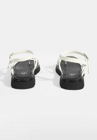 Witte sandalen met verstelbare banden, vlakke zwarte loopzool en een getextureerde zwarte binnenzool. Ontworpen voor comfort en draaggemak.