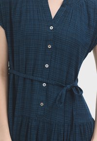 Blau kariertes Kleid mit kurzen Ärmeln, V-Ausschnitt, Knopfleiste, gebundenem Taillengürtel und Rüschensaum, hergestellt aus leichtem Stoff.