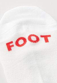 Hvit sokk med rød brodert tekst "FOOT" på oversiden, med en teksturert overflate og et klassisk atletisk design.