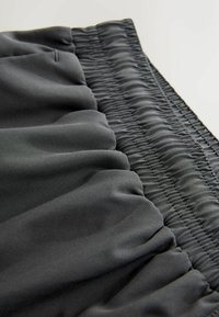 Ciemnoszara tkanina o gładkiej fakturze, z marszczonym elastycznym wykończeniem na krawędzi. Projekt jest miękki i zwiewny.