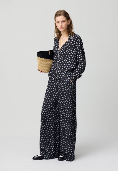 Completo due pezzi con stampa floreale nera composto da una camicia con bottoni e pantaloni a gamba larga. Indossato con una borsa a tracolla in tessuto intrecciato e sandali neri.