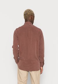 Brown corduroy shirt with long sleeves, buttoned cuffs, a pointed collar, and a curved hem, featuring a smooth texture and subtle shine.