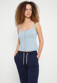 Camisola de alças azul-claro com riscas, com alças ajustáveis e botões centrais, combinada com calças de treino azul-marinho com cordões brancos e bolsos.