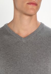 Szary sweter w serek wykonany z miękkiego materiału o delikatnym splocie, z gładką fakturą i subtelnym ryflowaniem wzdłuż kołnierza.