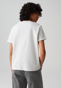 Graues kurzärmeliges Baumwoll-T-Shirt mit lockerer Passform und aufgerollten Ärmeln, das eine einfache, glatte Textur ohne sichtbare Muster aufweist.