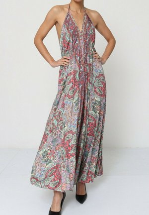 Femme portant une robe longue à col licou à motif cachemire coloré, les mains sur les hanches, se tenant devant un fond uni.