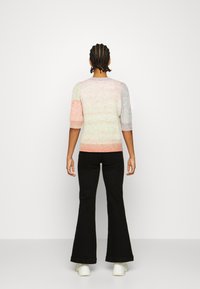Maglione lavorato a maglia in colori pastello con motivo testurizzato, maniche a palloncino corte e bordo a costine, abbinato a pantaloni neri a zampa d'elefante e sneakers bianche.