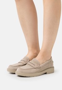 Beige semišové mokasíny s kulatou špičkou, prošitím a nízkou platformovou podrážkou. Mají klasický design s penny slotem.