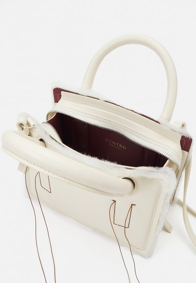 Cream leather handbag with a textured, fur-lined interior. Features zip closure, short handles, and brown stitching accents. Interior label visible.