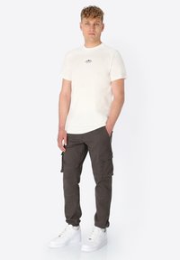 Cream short-sleeve t-shirt with small black logo, paired with dark cargo pants featuring side pockets and white sneakers.