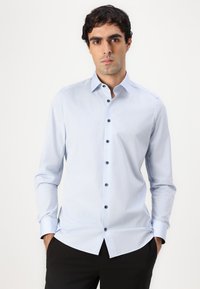 Chemise bleu clair avec un col boutonné, manches longues et boutons foncés. Tissu lisse avec une coupe ajustée et un ourlet droit.