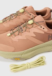 Chaussures de randonnée Hoka en pêche et beige avec un tissu texturé, des semelles en caoutchouc et des lacets jaunes. Présente le logo "Vibram" sur la semelle.
