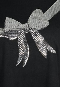 Schwarzes Oberteil aus Stoff mit einem großen silbernen Pailletten-Bow-Design, das eine strukturierte Oberfläche und Bandenden aufweist und somit einen dekorativen Akzent setzt.