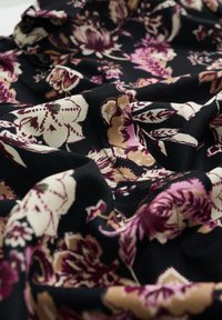 Svart tyg med blommönster med stora rosa, krämfärgade och vinröda blommor. Mjuk textur med draperade veck som visar intrikata detaljer.