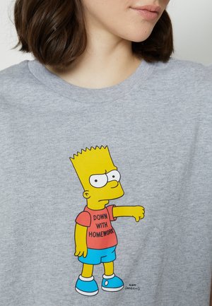 T-shirt en coton gris présentant un personnage de dessin animé, Bart Simpson, portant un t-shirt rouge avec le texte « DOWN WITH HOMEWORK » et un short bleu.