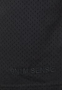 Tissu sportif noir avec un motif texturé et perforé. Présente un subtil détail brodé indiquant "9N1M SENSE."