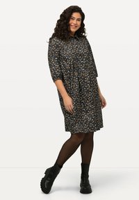 Vestito nero a fiori con fiori arancioni e bianchi, lunghezza al ginocchio, vestibilità ampia con colletto e maniche a tre quarti, abbinato a stivali neri.