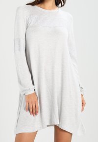 Abito grigio chiaro a maniche lunghe con tessuto strutturato, dettaglio in pizzo sul petto e una silhouette ampia e fluida con spacchi laterali.