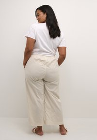 Pantaloni a gamba larga leggeri, di colore crema, con cintura elastica; abbinati a una maglietta bianca semplice. Texture liscia e morbida.
