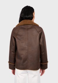 Brązowa skórzana kurtka z beżowym, miękkim kołnierzem z sztucznego futra. Luźny krój z widocznym przeszyciem i detalami przy mankietach. Minimalistyczny design.