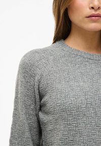 Maglione grigio a maglia con un motivo testurizzato, scollo rotondo e maniche raglan, che evidenzia un aspetto morbido e accogliente.
