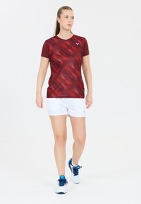 Rød mønstret trænings t-shirt med korte ærmer, parret med hvide shorts og marineblå sneakers med turkise accenter.
