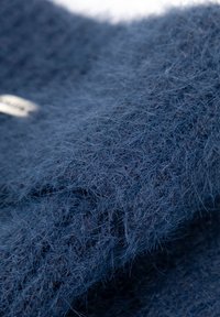 Tmavě modrá pletenina s měkkou texturou, obsahující jemná vlákna a hebký vzhled. V materiálu je viditelná malá cedulka.