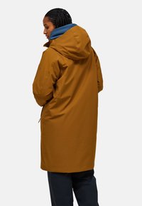 Waterproof bruine parka met een blauwe capuchon, heeft een relaxte pasvorm, ritssluitingen en een trekkoord in de taille voor aanpassing.