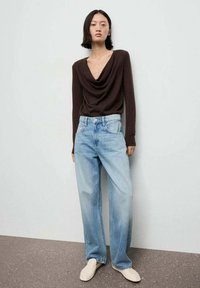 Bruine coltrui met lange mouwen, gecombineerd met lichtblauwe high-waisted wijde jeans; model draagt crèmekleurige instap schoenen. Zachte textuur.