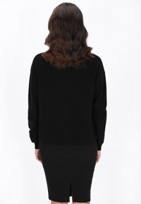 Maglione nero a maglia con spalle scese e polsini a coste, abbinato a una gonna nera aderente con spacco sul retro. Texture liscia.