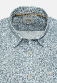 Camisa de manga corta azul claro con un patrón de olas, cierre de botones y un cuello interior amarillo en contraste. El material es tejido.