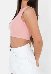 Top corto rosa a coste con scollatura rotonda, design aderente e spalline larghe, abbinato a pantaloncini di jeans bianchi con orlo sfrangiato.