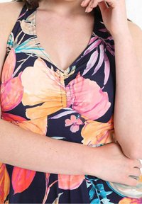 Robe fleurie avec un fond bleu marine, des fleurs vives roses et orange, un col en V et un détail froncé au niveau de la poitrine.