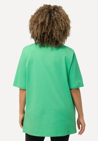 Zelené oversized tričko s krátkým rukávem, vyrobené z hladké bavlněné tkaniny a s kulatým výstřihem, zobrazené ze zadní strany.