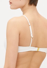 Hvit bikinitopp med ribbet tekstur, justerbare stropper med forgylte detaljer og en krok-lukking bak.