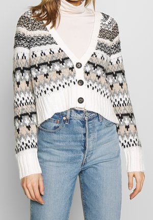 Cardigan en tricot crème et beige avec des motifs géométriques noirs et gris, décolleté en V profond, ourlet côtelé et quatre grands boutons noirs.