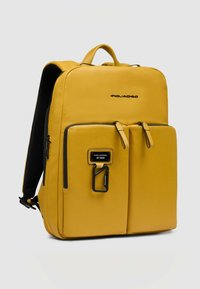 Gele leren rugzak met een gestructureerd ontwerp, twee voorzakken, ritssluitingen en zwarte metalen accenten. Gevoerde schouderbanden en rugpaneel.