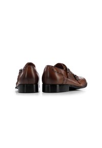 Zapatos de cuero marrón con un acabado pulido, que presentan una correa decorativa y hebilla, sutiles detalles de brogue y un tacón bajo negro.