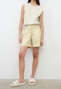 Krämfärgad ribbad ärmlös topp kombinerad med ljusgula skräddarsydda shorts; fluffiga vita slip-in-sandaler med svart text. Enkel och minimalistisk design.