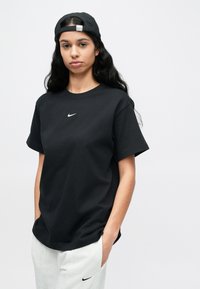 Juoda medvilninė trumpomis rankovėmis marškinėliai su apvalia iškirpte, ant krūtinės mažas baltas Nike logotipas; derinami su pilkomis sportinėmis kelnėmis.