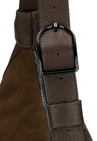 Bruine suède schoudertasriem met een accent van getextureerd leer en een matzwarte metalen gesp. Voorzien van een zichtbare rits aan de zijkant.