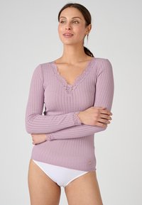 Top lungo a maniche ribattute di color lilla con scollatura a V in pizzo ondulato e polsini in pizzo. Presenta un piccolo logo del marchio sull'orlo. Abbinato a biancheria intima bianca.
