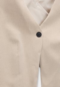 Blazer beige à rayures fines avec un décolleté en V, une fermeture par un bouton noir unique et une doublure lisse. Le tissu présente une texture subtile.